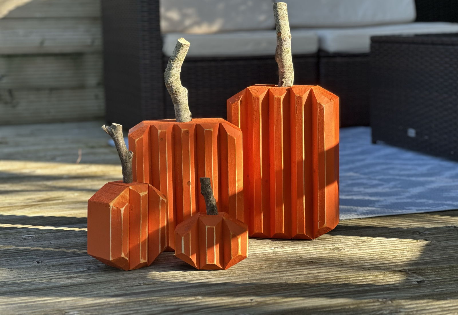 Three faceted wooden pumpkins in pumpkin orange, each with a real branch stem, standing on a garden deck in low afternoon sun.