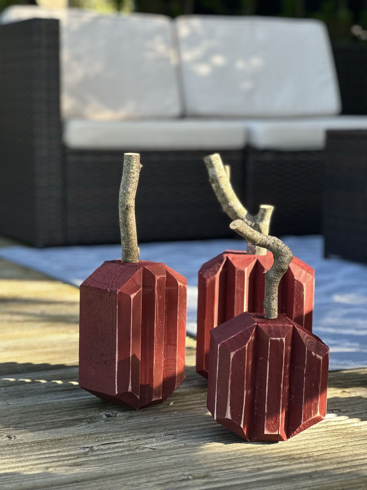 Three burgundy wooden pumpkins with real branch stems on a deck in evening light.
